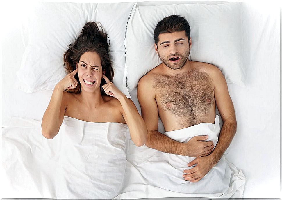 Couple in bed with man snoring and woman covering her ears.