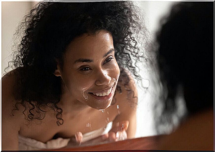 Woman washing her face in front of the sink mirror.